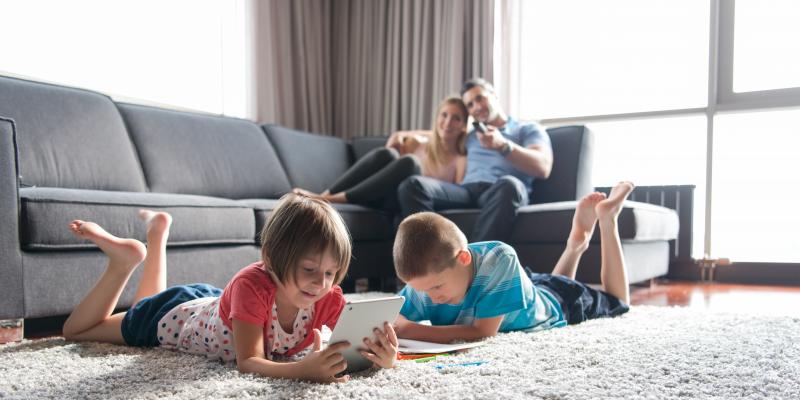 Kids playing on their iPads in a living room with parents watching