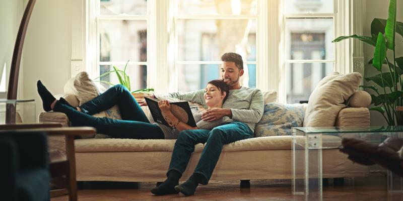young couple laying on sofa reading in bright room